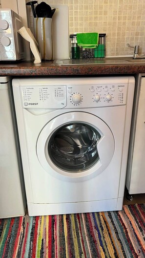Eine Waschmaschine mit Frontlader und Bedienfeld, eine Küchenarbeitsplatte mit eingebauter Mikrowelle und ein Streifen Teppich.