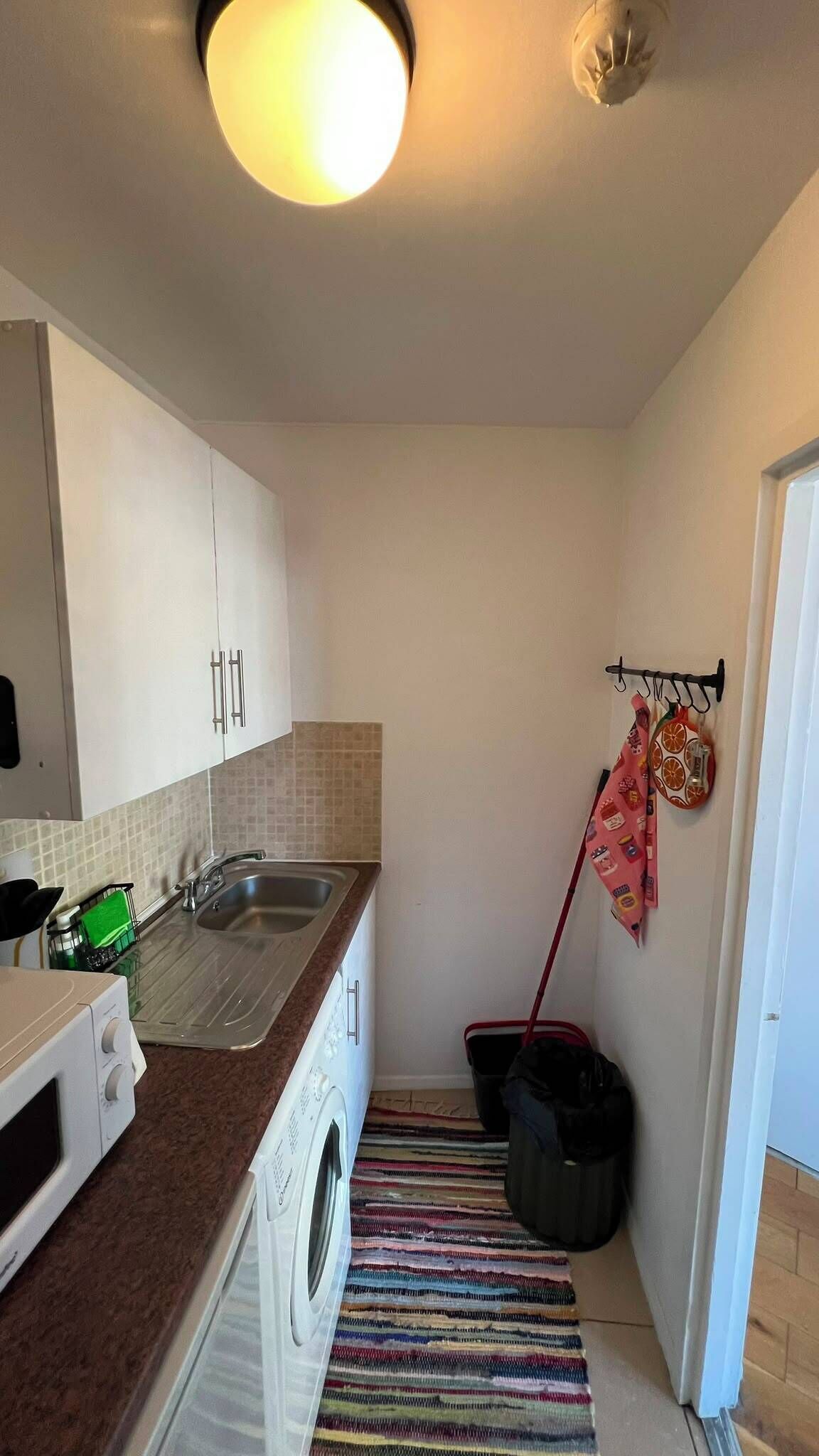 A compact kitchen with a washing machine, a sink, and a striped rug.