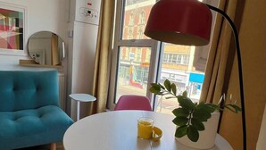 Un salon moderne avec un canapé turquoise, une table ronde blanche surmontée d’une lampe rouge et des chaises roses.