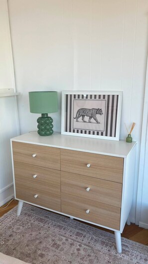 Eine weiße Kommode mit Schubladen, eine grüne Lampe und ein gerahmtes Bild eines Tigers darauf.