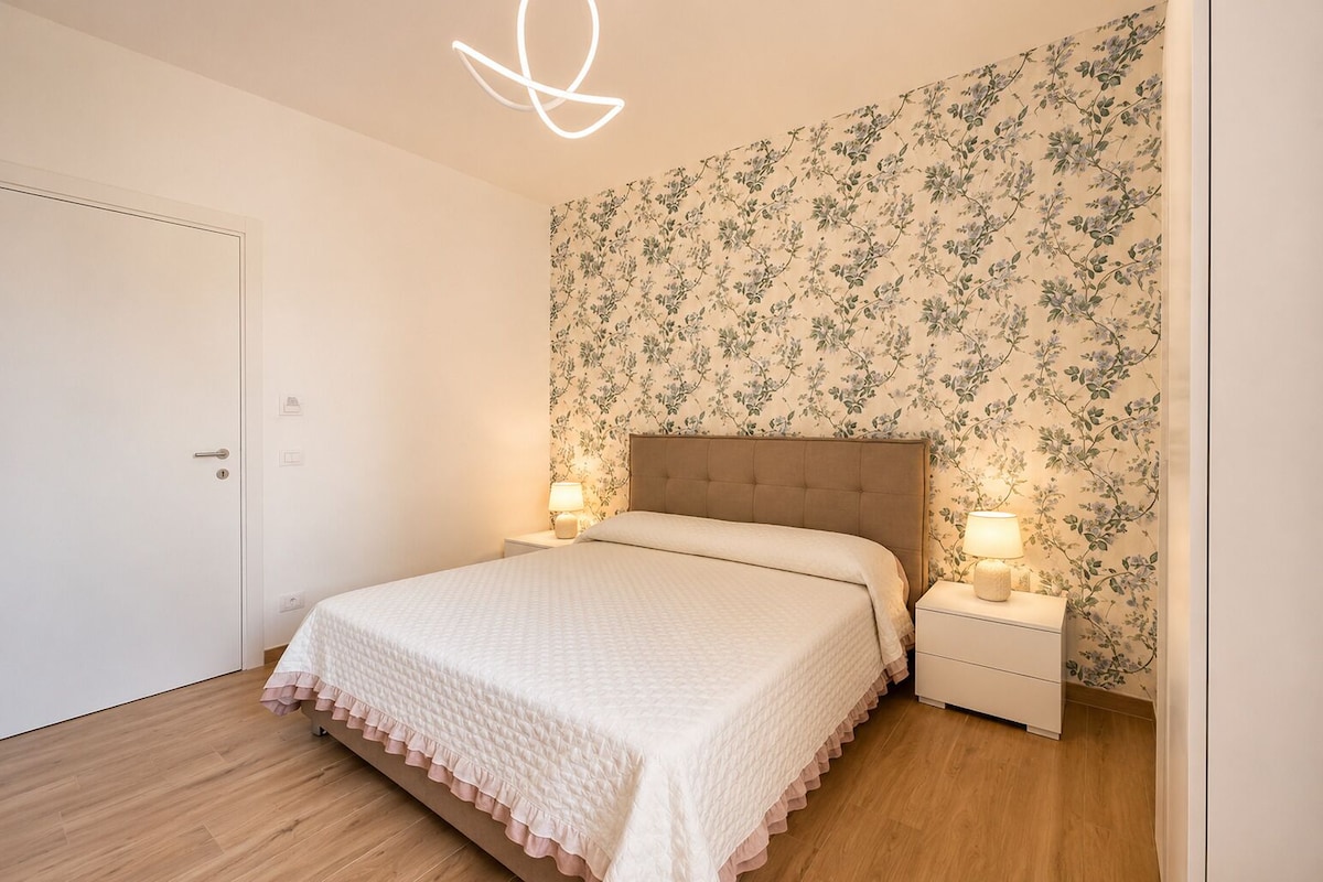 Una camera da letto con un letto, comodini, una porta e carta da parati a motivi floreali.