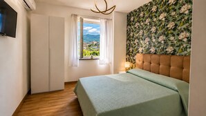 A bedroom with a bed, a window with a view, a wall-mounted TV, and a ceiling light fixture. - B&B Venere Rooms  (Pimonte)