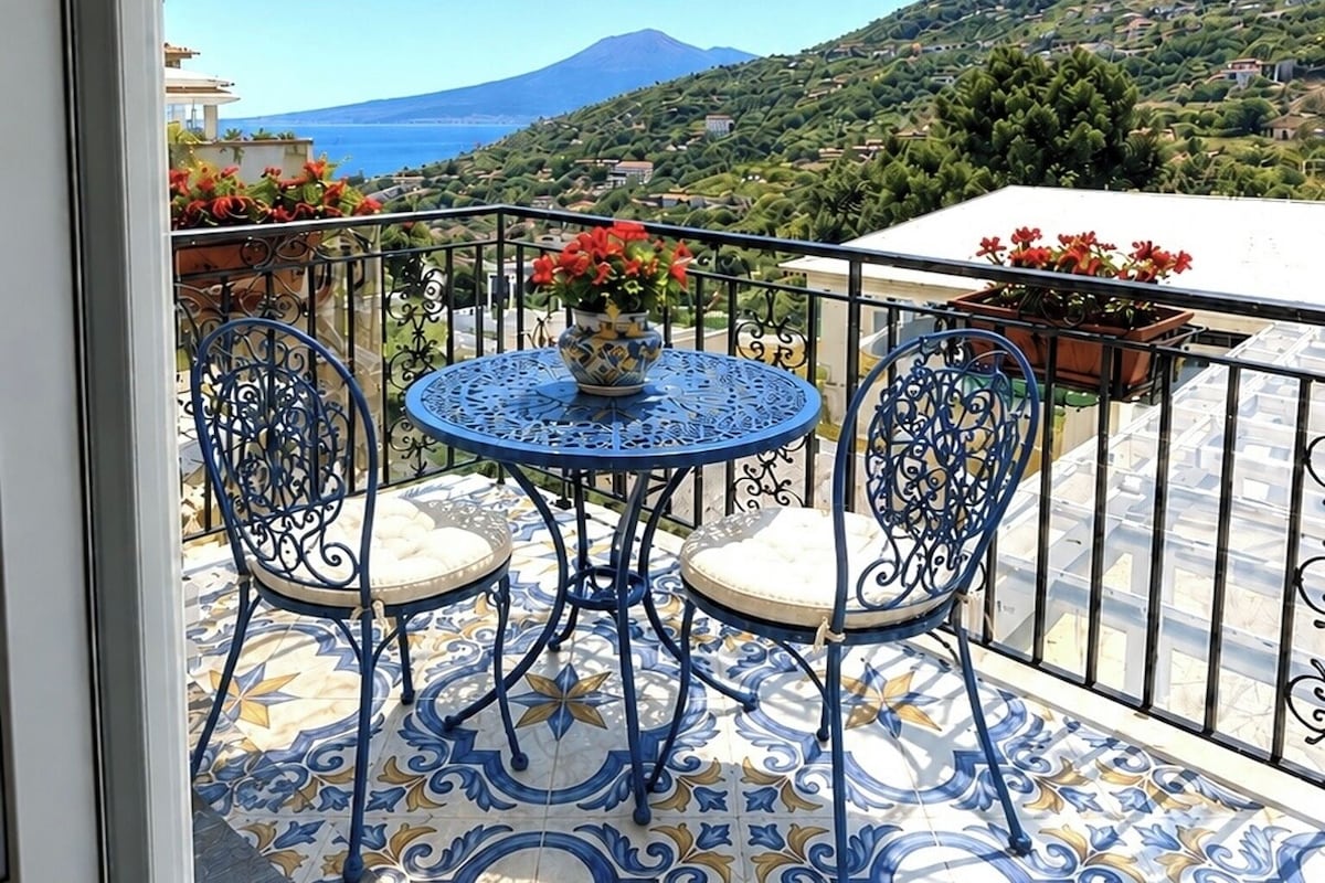 Un balcone con un tavolo rotondo e sedie, vista su una montagna e pavimento piastrellato.