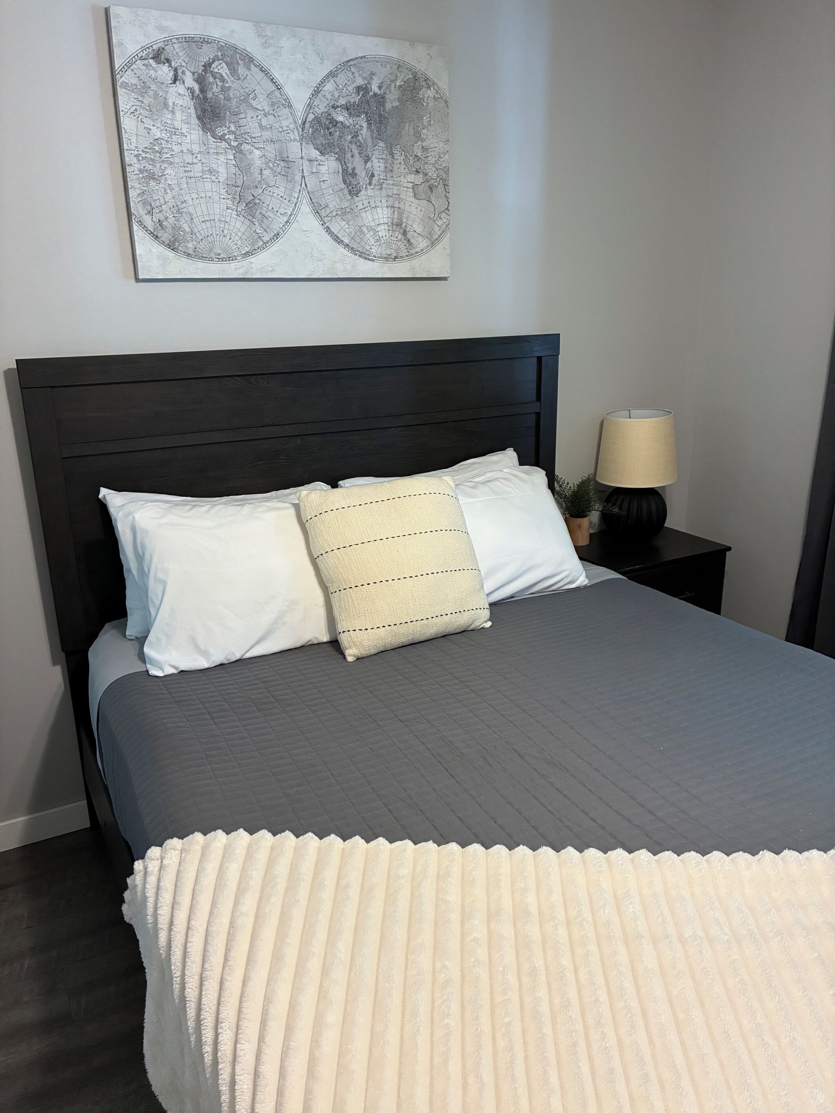 Un lit bien fait, avec une tête de lit sombre, des oreillers blancs et beige, et une couvre-lit grise matelassée.