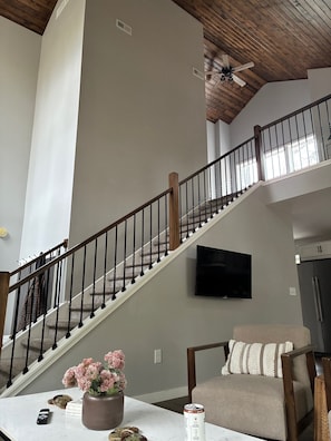 A staircase with a wooden railing, a flat-screen TV mounted on the wall, and a dining area with a table and chairs. - Newly Remodeled Modern house with AC in Crosslake w/ Firepit and Free Wood (Crosslake)