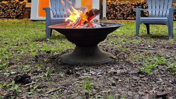 A house with a fire pit in the front yard, two Adirondack chairs, and a stack of firewood.