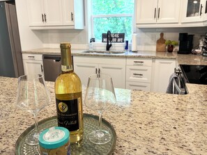 A kitchen with white cabinets, a granite countertop, a wine bottle, and two wine glasses on a glass tray. - HOT TUB! New 2027  - Newly Remodeled Modern house with AC in Crosslake (Crosslake)