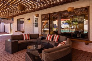 A covered outdoor seating area with wicker furniture and a glass wall overlooking a pool. - Havasu Acoma - Pool, Spa, Game Room, Sleeps 16 (Lake Havasu City)