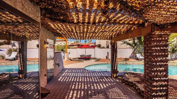 Ein Poolbereich mit einer Pergola, einer Backsteinmauer und Blick auf einen Pool und Gartenmöbel.