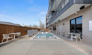A pool area with lounge chairs and tables, a wooden fence, and a building with a sign indicating no diving. - DallasHaus | Pool & Gym, Love Field (Dallas)
