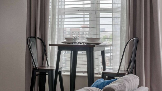 Een kamer met een raam, een tafel met een glas, twee stoelen en een bed.