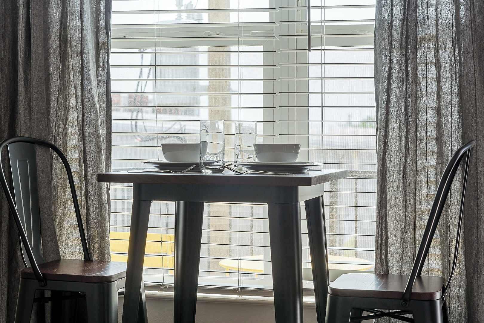 A dining table with two chairs, a window with blinds, and a view of the street outside.