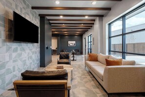A modern living room with a sofa, armchairs, a coffee table, and a flat-screen TV mounted on the wall. - DallasHaus | Pool & Gym, Love Field (Dallas)