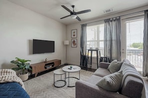 Ein Wohnzimmer mit Flachbildfernseher, Deckenventilator, einer Couch, einem Couchtisch und einem Essbereich mit Tisch und Stühlen.