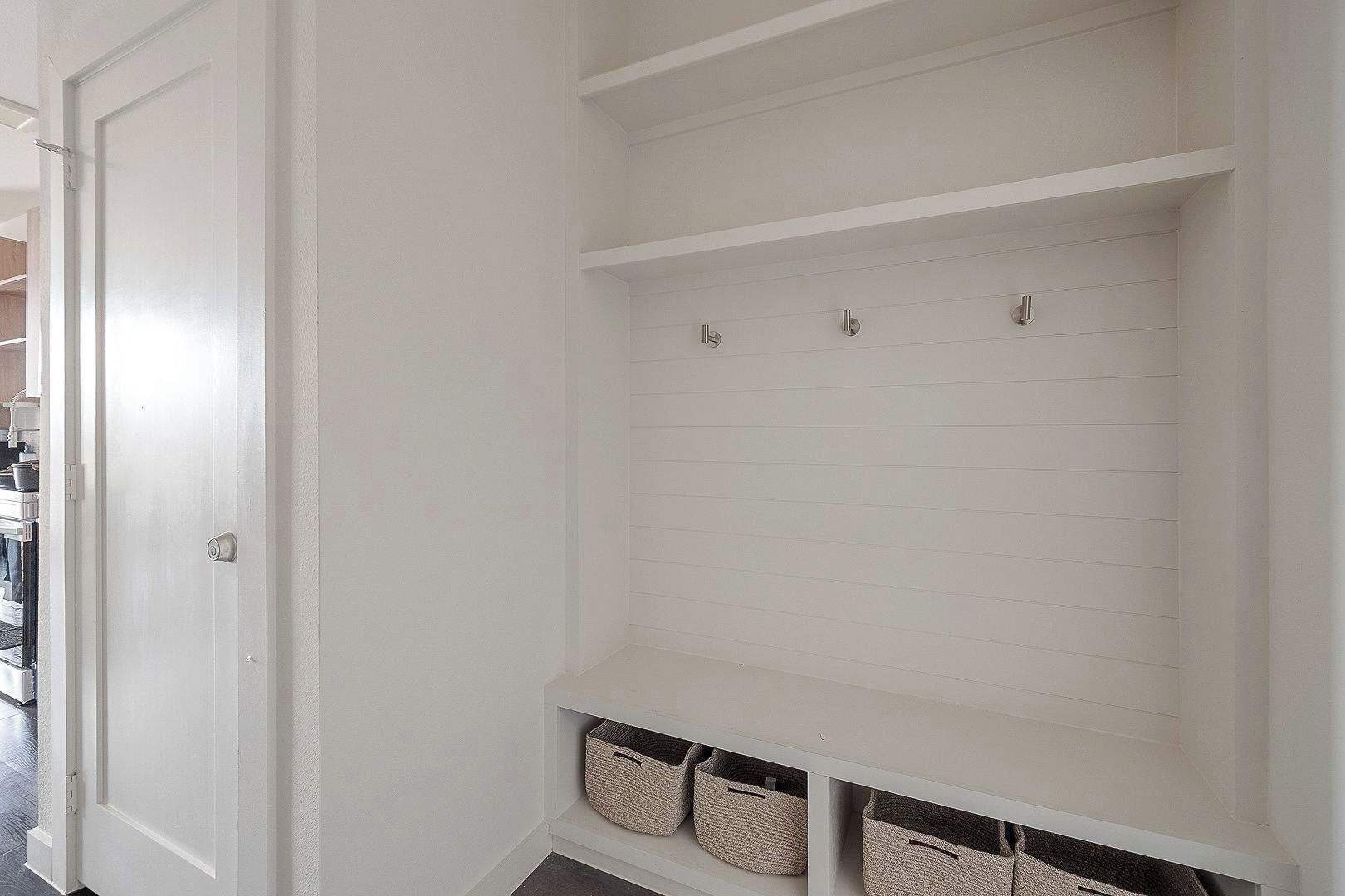 A white interior with a door, a shelf unit with baskets, and a tiled floor.