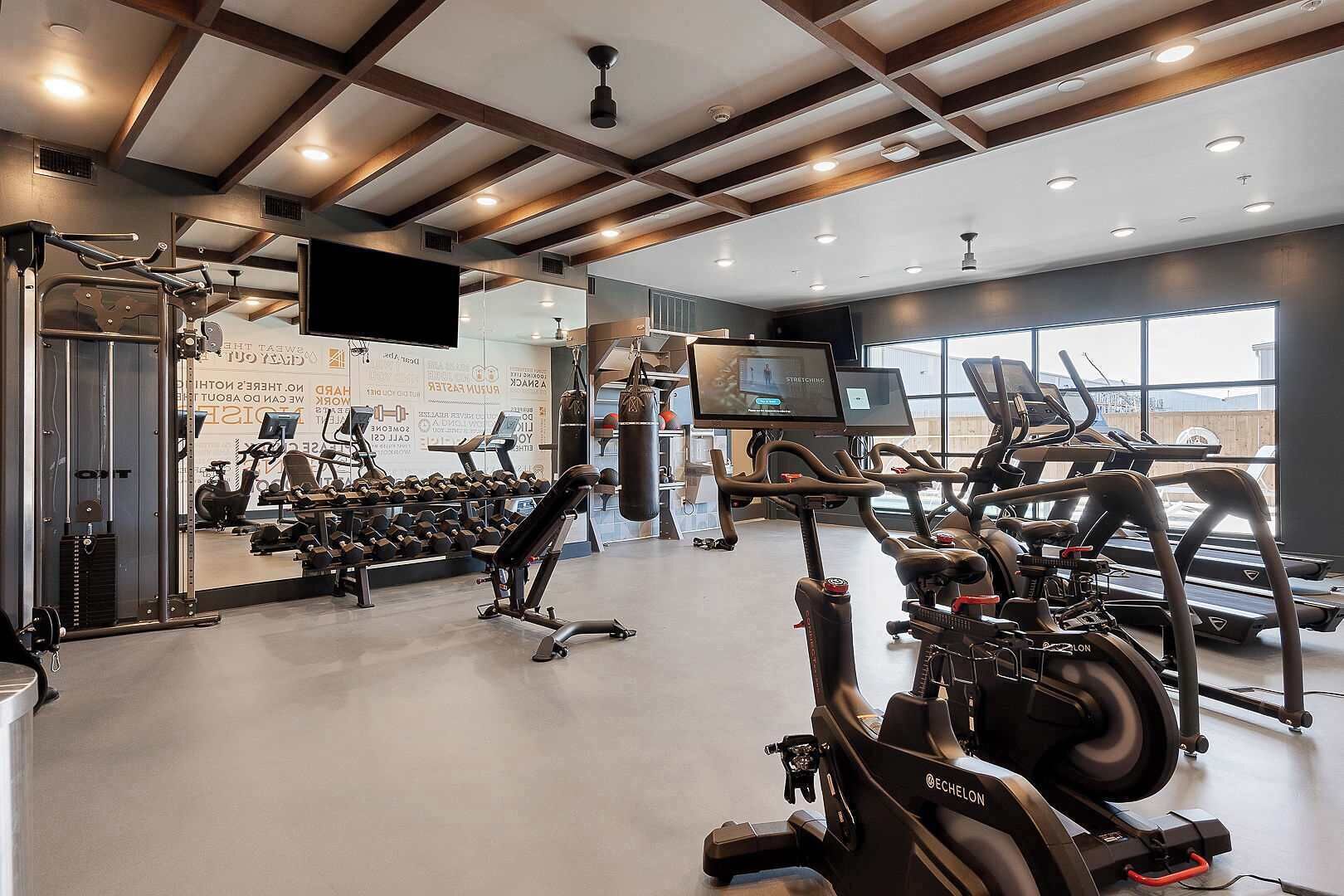 A gym with cardio machines, weightlifting equipment, and a large mirror.