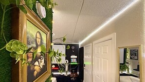 Um corredor com uma obra de arte emoldurada, uma porta e um espelho refletindo um quarto com um sofá branco.