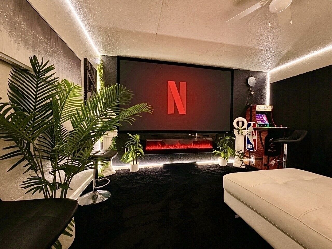 Ein modernes Wohnzimmer mit einem großen Flachbildfernseher, der das Netflix-Logo anzeigt, einer bequemen Couch, einem Couchtisch und einem kleinen Basketball-Arcade-Spiel.
