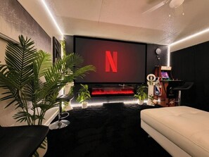 Uma sala de estar moderna com uma televisão de tela plana grande exibindo o logotipo da Netflix, uma lareira e uma área de estar aconchegante.