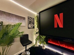 Una sala de estar moderna con un televisor de pantalla plana grande, un sillón de cuero negro y una chimenea con detalles rojos.