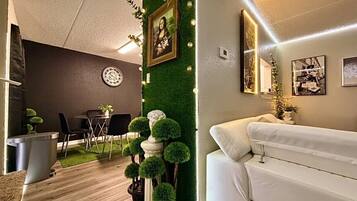 A modern living room with a white sofa, a dining area with a round table and chairs, and a green wall with a framed picture.