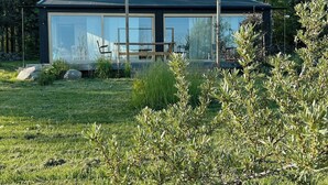 Een modern glazen huis met een plat dak, omgeven door een gazon met rotsen en struiken.