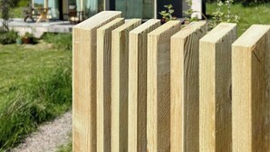Een modern huis met een glazen gevel, een houten hek op de voorgrond en een heldere lucht.