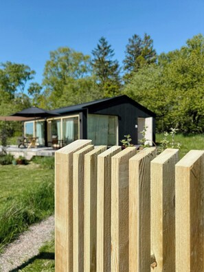 Une maison moderne avec une façade en verre, une clôture en bois au premier plan et un ciel dégagé.