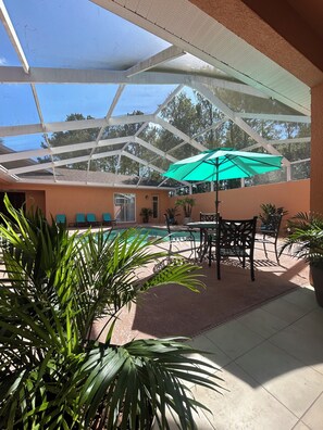 A covered outdoor area with a pool, chairs, and umbrellas.