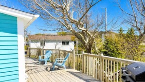 Une terrasse en bois avec deux chaises, un barbecue et un bâtiment blanc orné de bordures bleues.