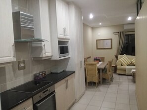 A modern kitchen with white cabinets, a black countertop, and a dining area with a table and chairs. - Cabanas on the Beach Warner Beach (Kingsburgh)
