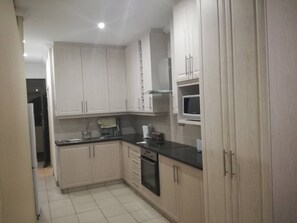 A kitchen with light-colored cabinets, a black countertop, a microwave, and a dishwasher. - Cabanas on the Beach Warner Beach (Kingsburgh)