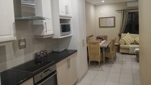 Een moderne keuken met witte kasten, een zwart aanrecht en een eethoek met een tafel en stoelen.