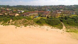 Een kustresort met meerdere gebouwen, een zandstrand en weelderige begroeiing.