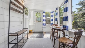 A room with a wooden bench, a table with chairs, a window with blue and white curtains, and a door with a heart-shaped decoration. - The Little Lighthouse (Sarnia)