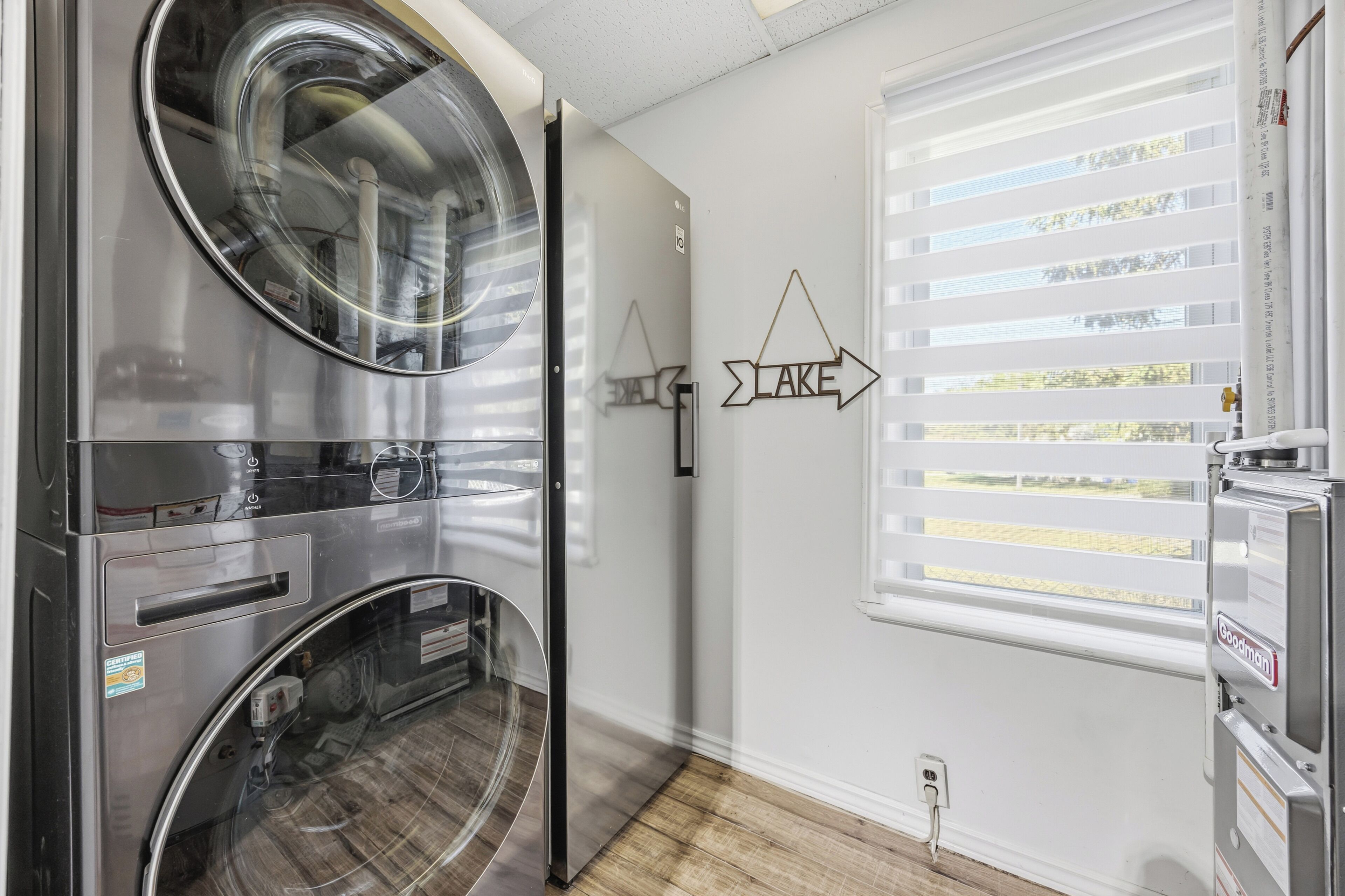 A laundry room with a front-loading washer and dryer, a window with blinds, and a wall-mounted sign pointing to the right.
