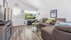 A living room with a brown sofa, a glass coffee table, a fireplace, and a window with a view of greenery. - The Little Lighthouse (Sarnia)