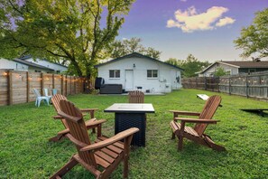 A backyard with a wooden deck, a table, and two Adirondack chairs. - East Austin Retreat w/ Hot Tub & Backyard (Austin)