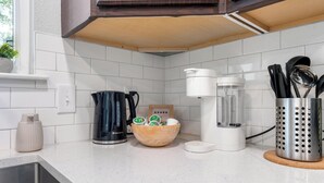 A kitchen with white tiles, a coffee maker, a blender, and a wooden bowl with green and white containers. - East Austin Retreat w/ Hot Tub & Backyard (Austin)