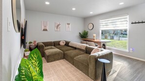 A modern living room with a sectional sofa, a round coffee table, and a large window with blinds. - East Austin Retreat w/ Hot Tub & Backyard (Austin)