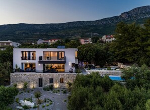 Ein modernes, zweistöckiges Haus mit Steinverkleidung, einem Balkon und einem Pool.