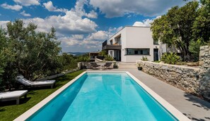 Ein modernes Haus mit Swimmingpool, Liegestühlen und einer Steinmauer.