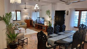 Una sala de estar con televisor, sofá, mesa de comedor, sillas, ventiladores de techo y plantas en macetas.