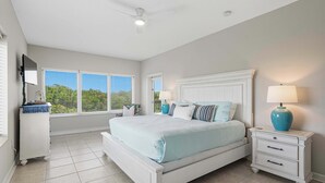 Un dormitorio con cama, mesitas de noche, televisor y ventanas.
