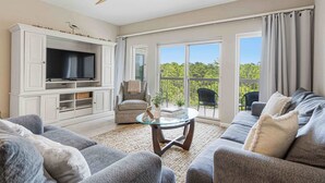 Una sala de estar con televisión, sofá, sillón y mesa de centro de vidrio.