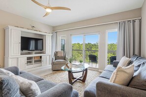 Ein Wohnzimmer mit Fernseher, Sofa, Sessel und Glastisch.