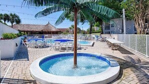 Zona de piscina con sillones de descanso, bañera de hidromasaje y una palmera.