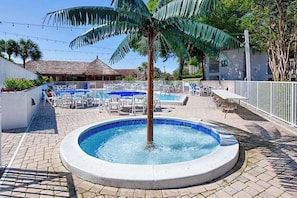 Ein Poolbereich mit Liegestühlen, einem Whirlpool und einer Palme.