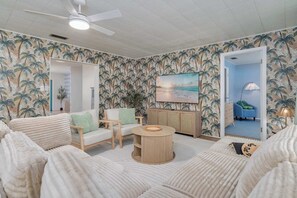 A room with a beach-themed wallpaper, a round wooden coffee table, a white sofa, and a painting of a sunset. - 4BR Tampa retreat w/ private pool (Tampa)