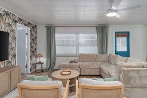 Ett vardagsrum med en soffa, ett litet runt bord, en tv och ett fönster med gardiner.